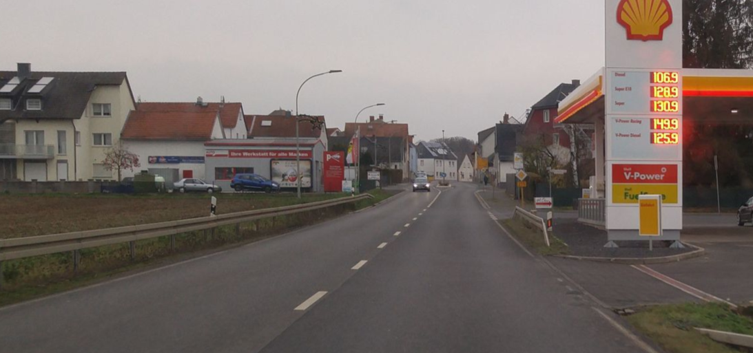 Eine zweispurige Ortsdurchfahrt mit Tankstelle auf der rechten Seite ist zu sehen.