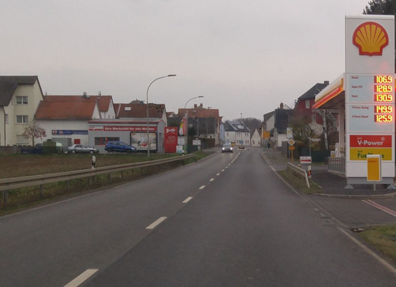 Eine zweispurige Ortsdurchfahrt mit Tankstelle auf der rechten Seite ist zu sehen.