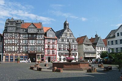 Auf dem Bild ist der Butzbacher Marktplatz mit Fachwerkhäusern, Rathaus und dem Brunnen in der Mitte zu sehen.
