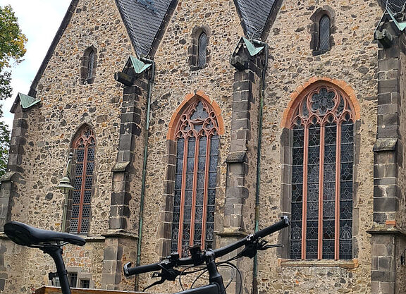 Ein Fahrrad steht vor der Kirche an eine Bank angelehnt. Auch Kirchen können, insbere Radwegekirchen setzen sich für das Fahrradfahren ein.